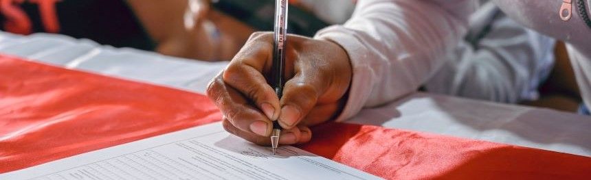 person signing a form that is sitting on a table that has a red and white table cover.