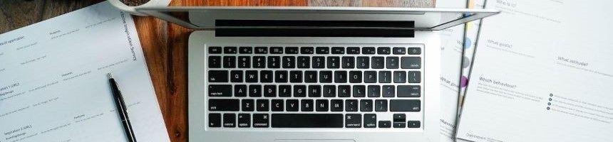 Open Laptop computer, paperwork, and a pen, sitting on a desktop with various paper documents