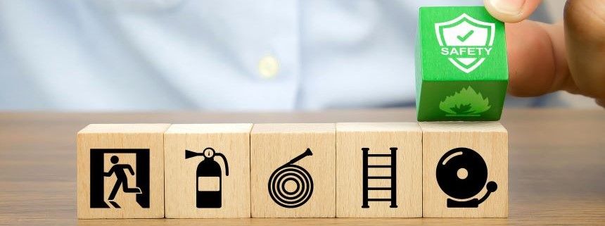 Close up of row of wooden blocks (with various icons denoting fire related topics) with  hand lifting a  green fire Safety wooden block