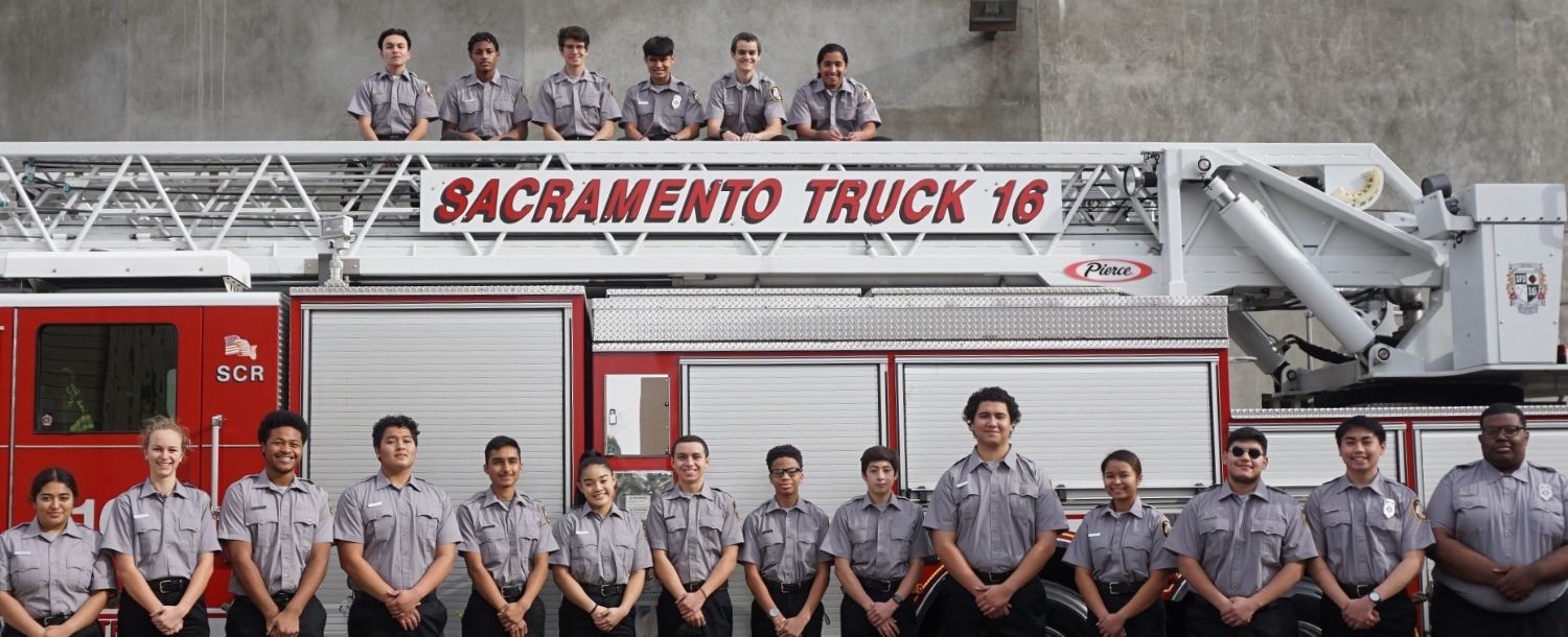 class photo of cadets standing on the side of a fire truck and on the ladder