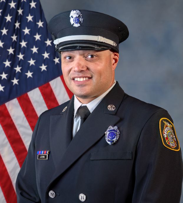 photo of captain justin sylvia in professional uniform with U.S. flag and gray background.