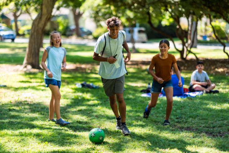 Teens playing soccer in a park, grass, trees