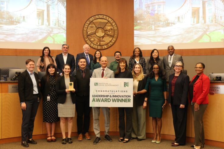 Large group photo at council chambers. Sign in center that says "Leadership & Innovation Award Winner"