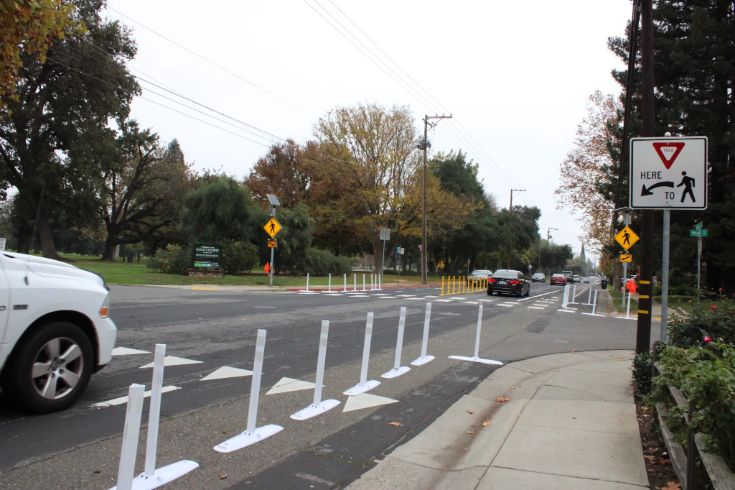 A street with new white bollards and pedestrian safety signs installed along a crosswalk.