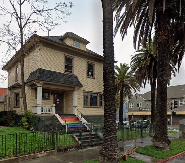 House, with rainbow painted stairs, palm trees, sidewalk, fence, grass
