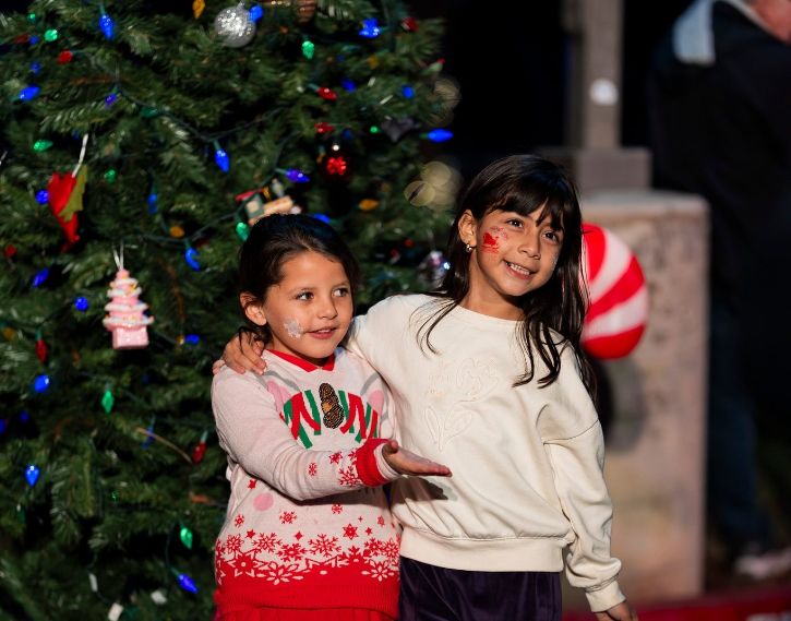 Two kids smiling for camera in front of decorated holiday tree