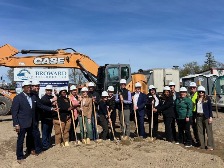 Sixteen people standing together for a group photo holding shovels and wearing hard hats