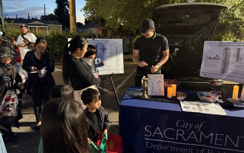 Staff at tabling event. City logo on table display, people talking, infographics displayed