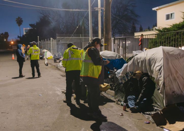 Volunteers wearing safety, reflective vests speaking to people at homeless encampments
