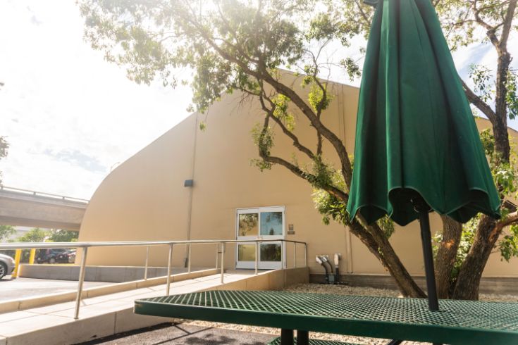 X Street shelter in Sacramento, tan building, table with green umbrella, tree