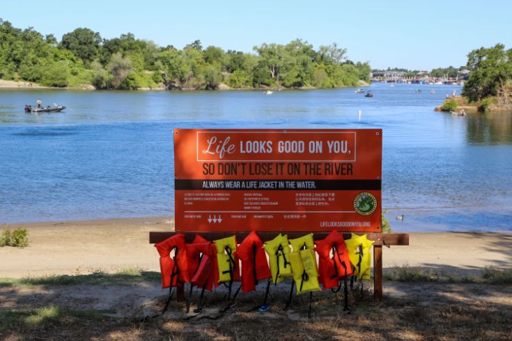 Life jackets at the river, sign with text "Life looks good on you so don't lose it on the river"