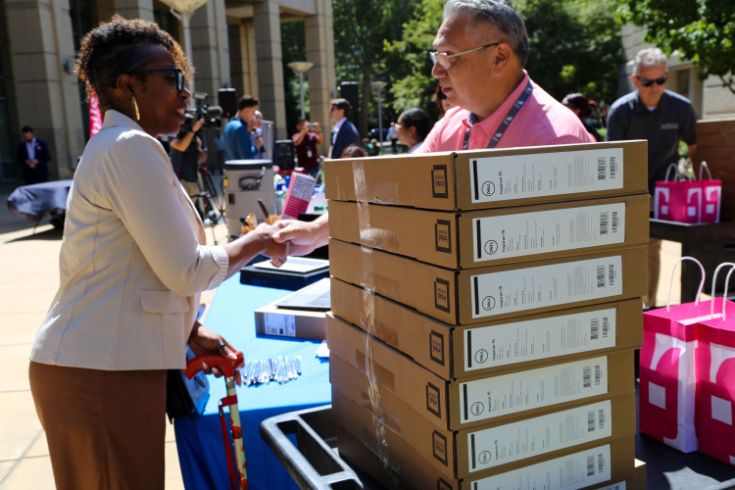 Two people shaking hands, large stack on new laptops