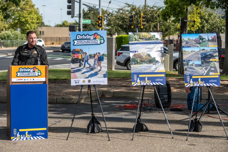 Police officer speaking at podium with "Driving ABCs" displays
