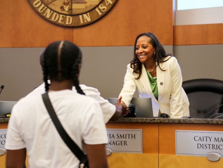 City Manager Maraskeshia Smith at City Council shaking hands with teenager at Dias