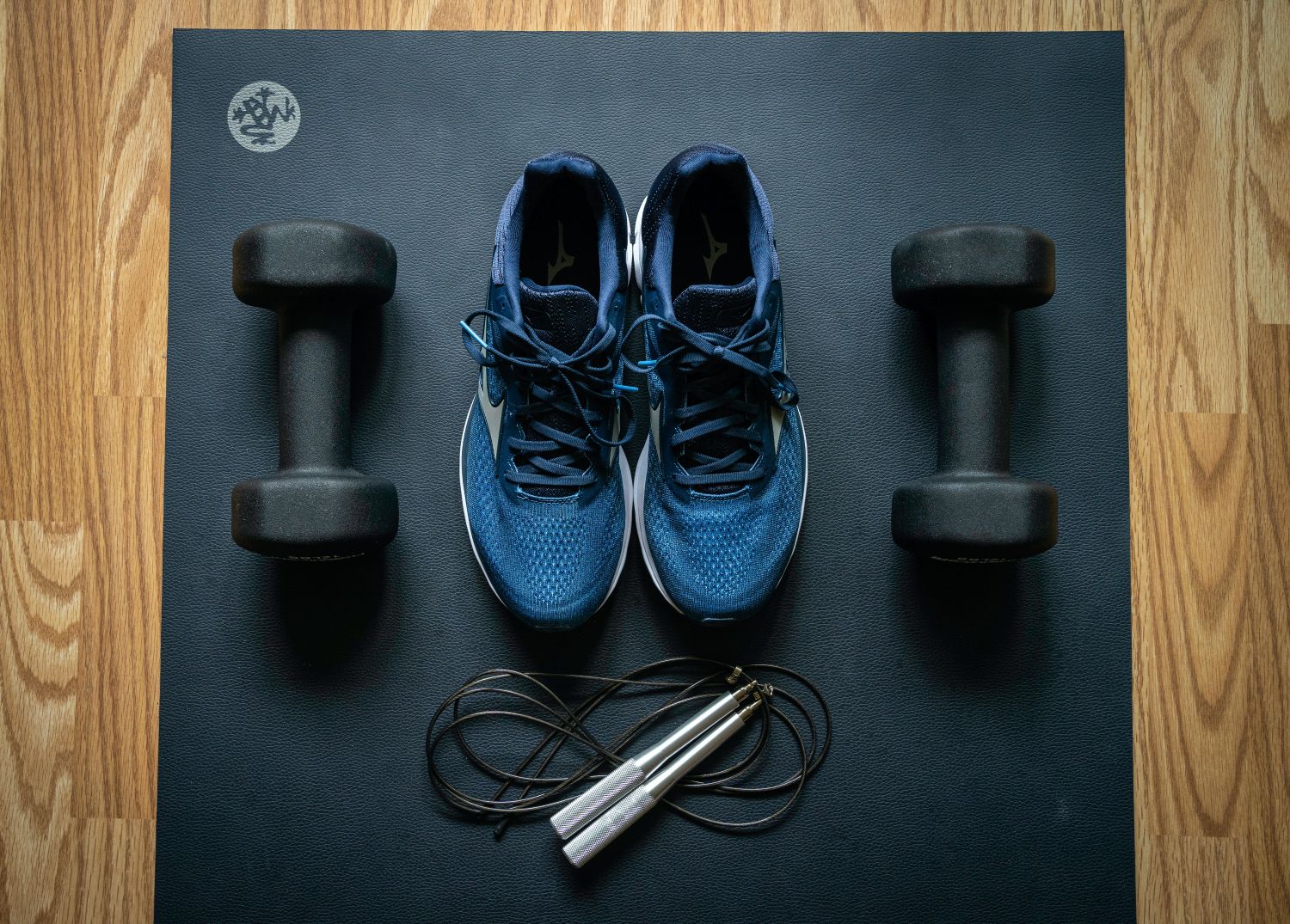 exercise mat with a pair of blue running shoes in the middle, a hand weight to either side of the shoes, and a jumprope in front of the shoes