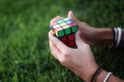 Two hands holding a rubix cube with a green lawn in the background.