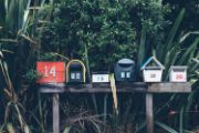 Row of mailboxes in different shapes and colors sitting on wood stand