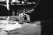 Person filling out forms with pen in right hand and holding documents with left hand