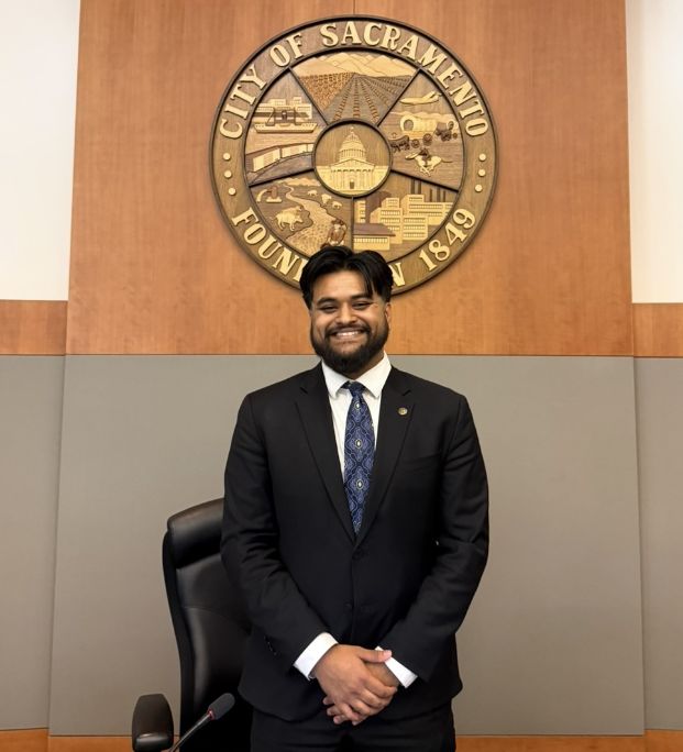 Photo of Sarim Malik standing in front of a City of Sacrameto seal wall plaque