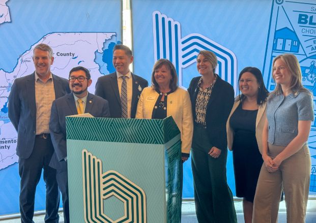 Image of local electeds and leaders who are a part of SACOG, the Sacramento Area Council of Governments. The group is standing around a podium. Councilmember Caity Maple is standing on the right.