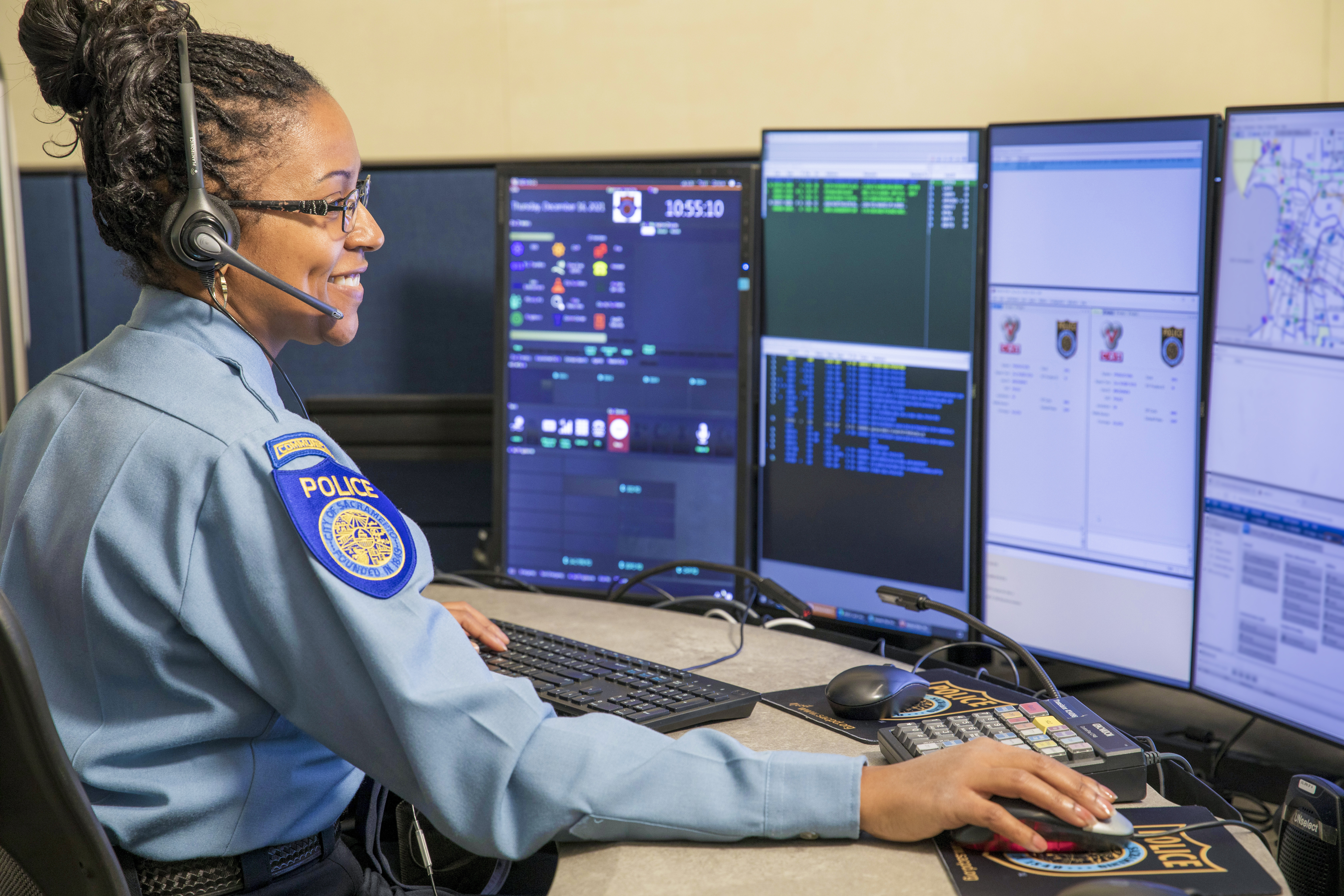 A photo of a Sacramento Police Department Dispatcher sitting at their workstation, with multiple screens mounted in front of them