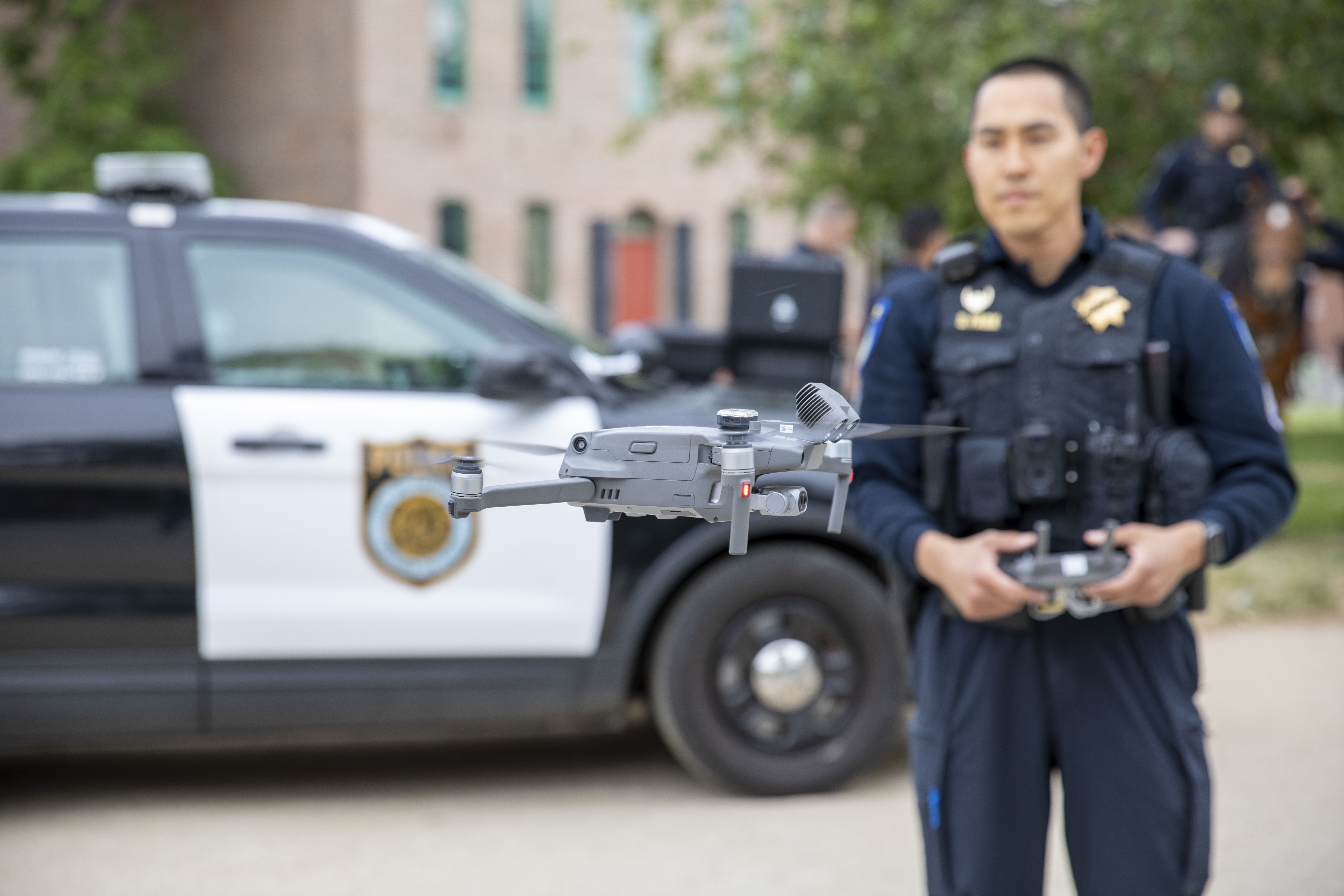 Photo of a Sacramento Police Department officer in full uniform flying an uncrewed aerial system in old Sacramento, with a Sacramento Police Department patrol vheicle visible in the background