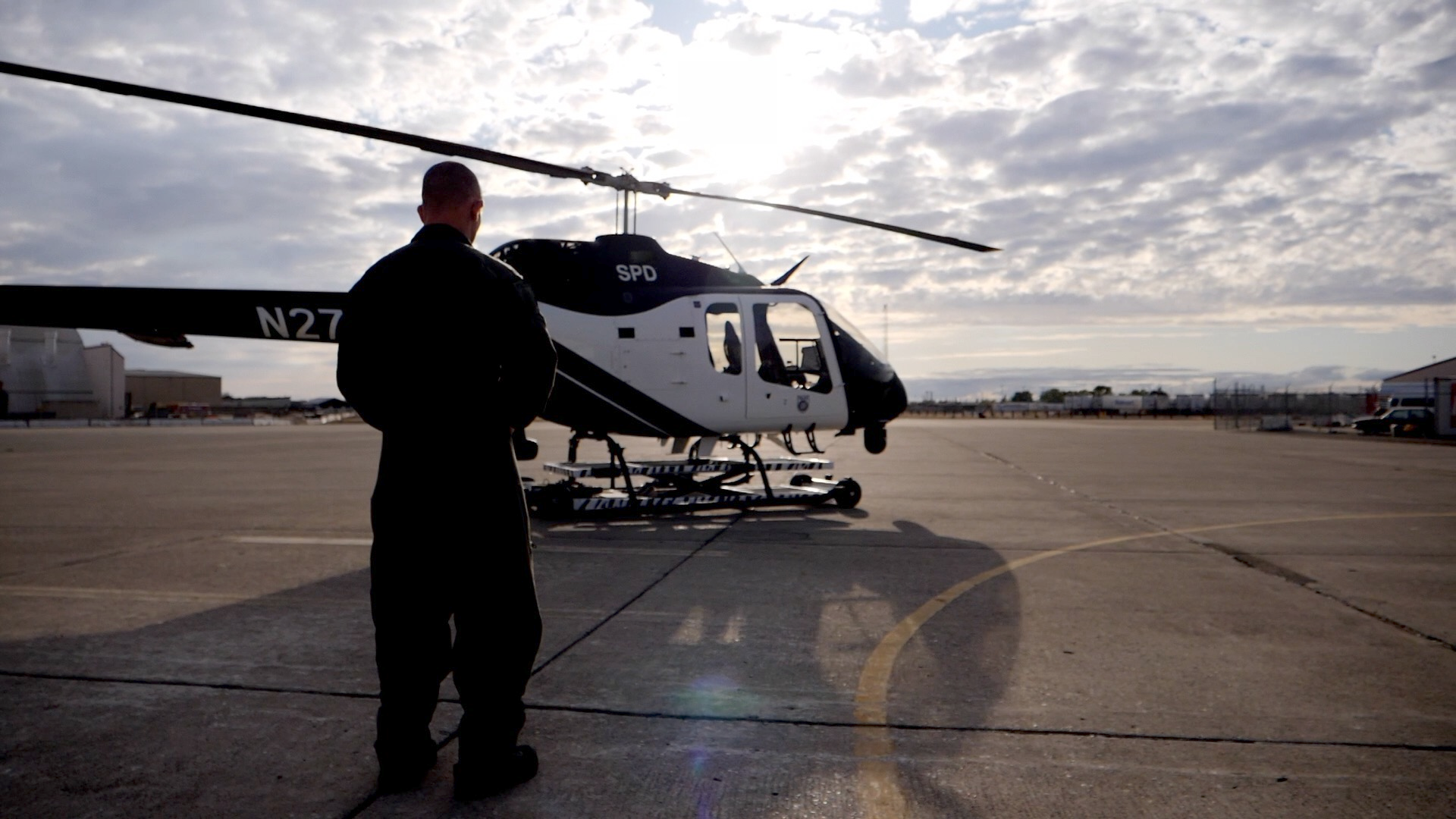 Photo of a Sacramento Police officer in their pilot's uniform, facing one of the Department's black and white helicopters in the background