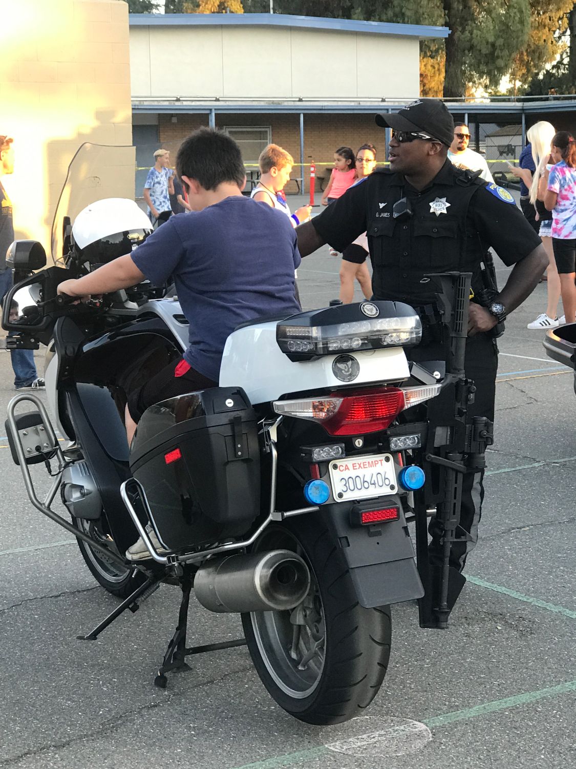 A photo of a traffic officer letting a child sit on his parked police motorcycle at a school event.