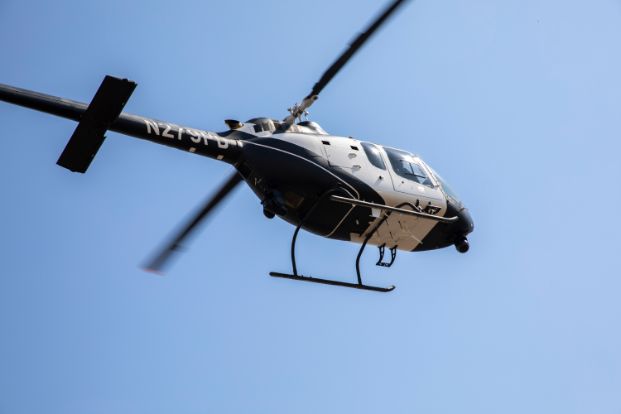 A photo of the Sacramento Police Department’s Air Unit Helicopter flying with a blue-sky background that is somewhat cloudy. The photos is taken from underneath the helicopter, so the bottom and one side are visible. The helicopter is black and white with the identifier “N279PD” painted on the tail.