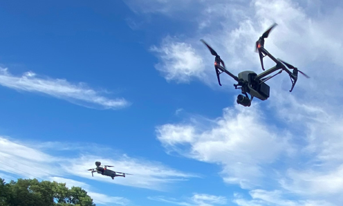 A photo of three Sacramento Police Department uncrewed aerial systems flying near each other with blue sky, clouds, and trees in the background.