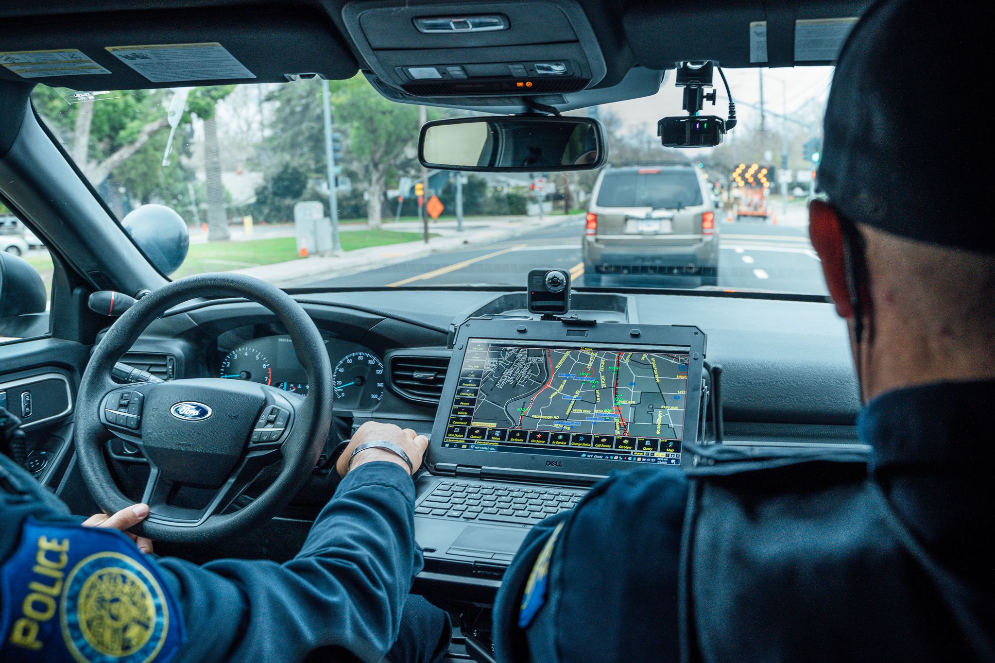 A photo off two officers on routine patrol in a police vehicle,  taken from the backseat of the car looking through the windshield, with a view of the back of the officers heads, their Sacramento Police uniform patches and in-car mounted computer's mapping system.