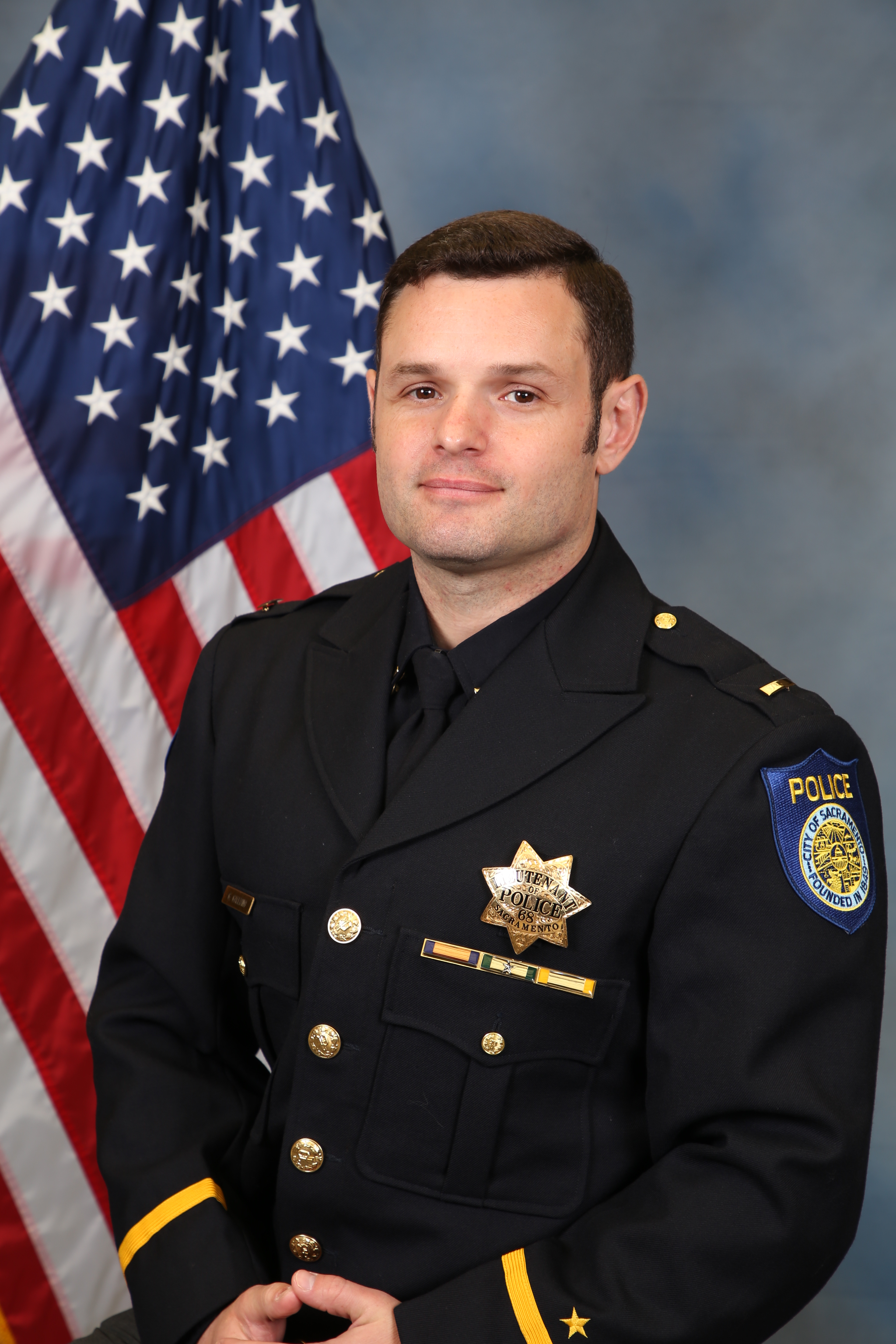 Photo of Greg Galliano in uniform standing in front of the American flag.