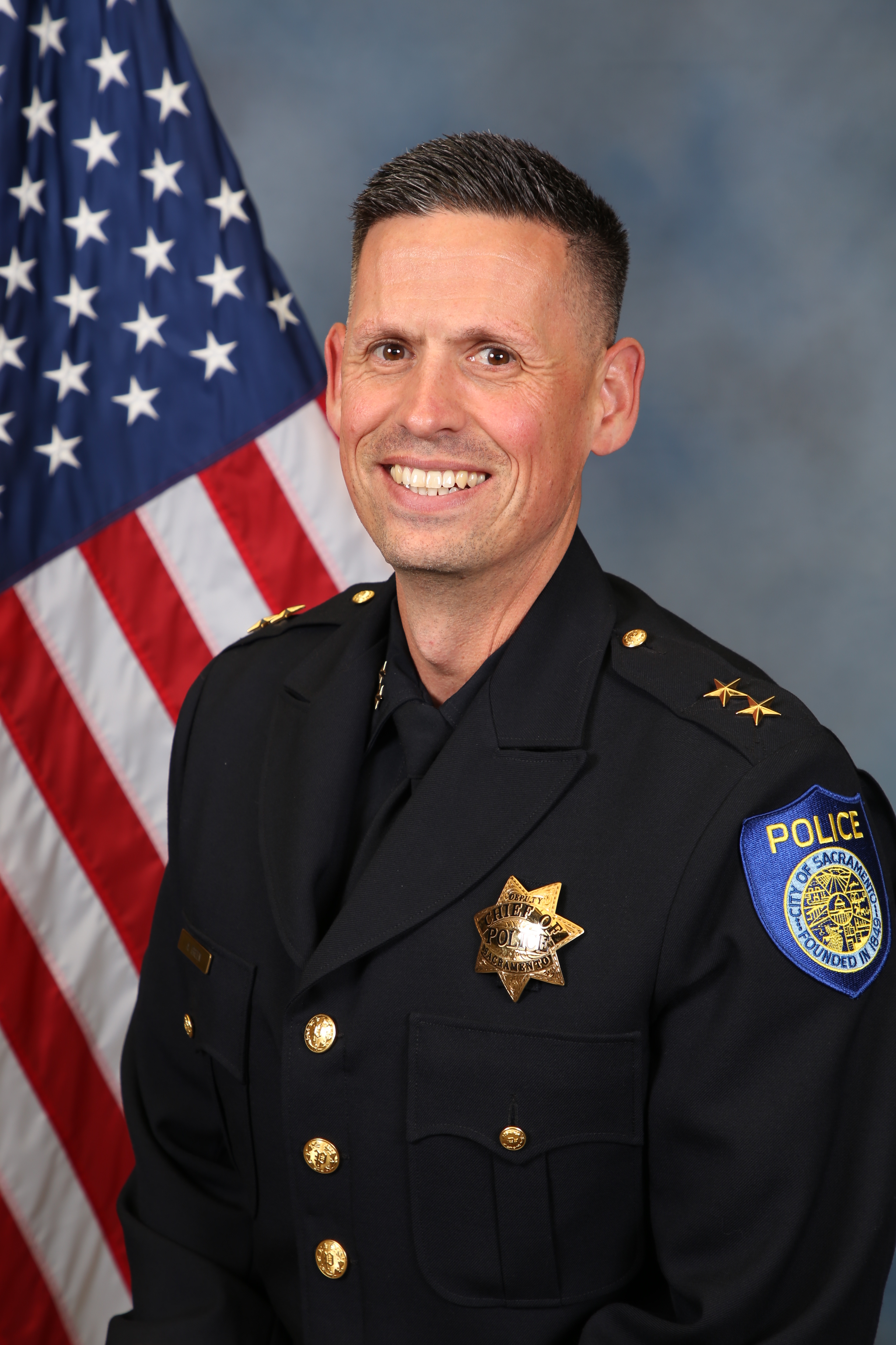 Photo of Deputy Chief Adam Green in uniform with the American flag in the background.