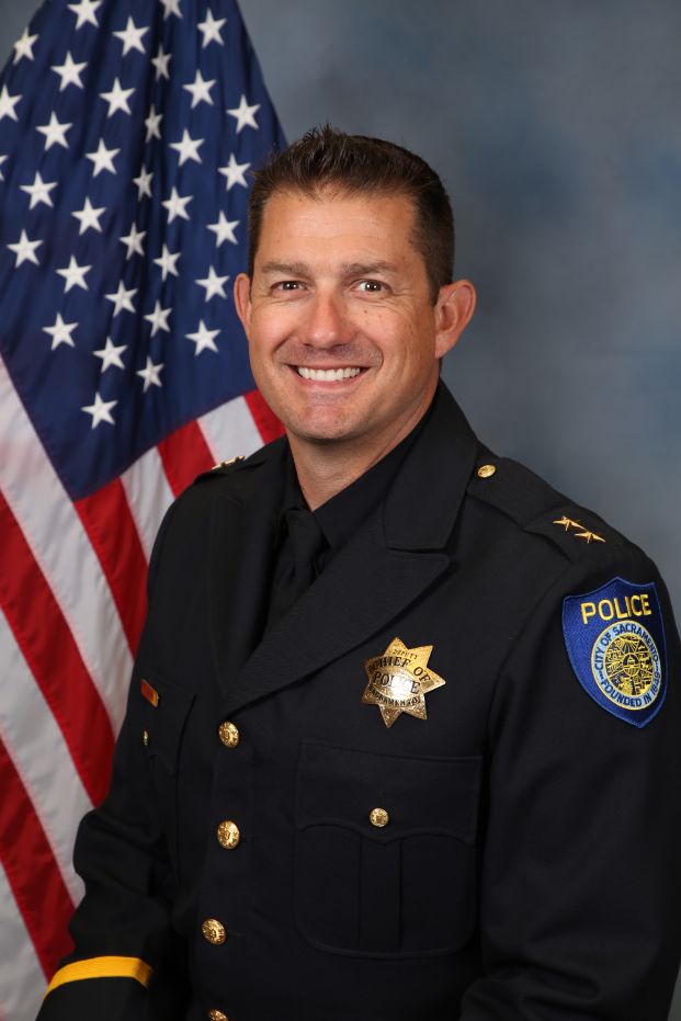 Photo of Deputy Chief Bryce Heinlein in uniform in front of the American flag