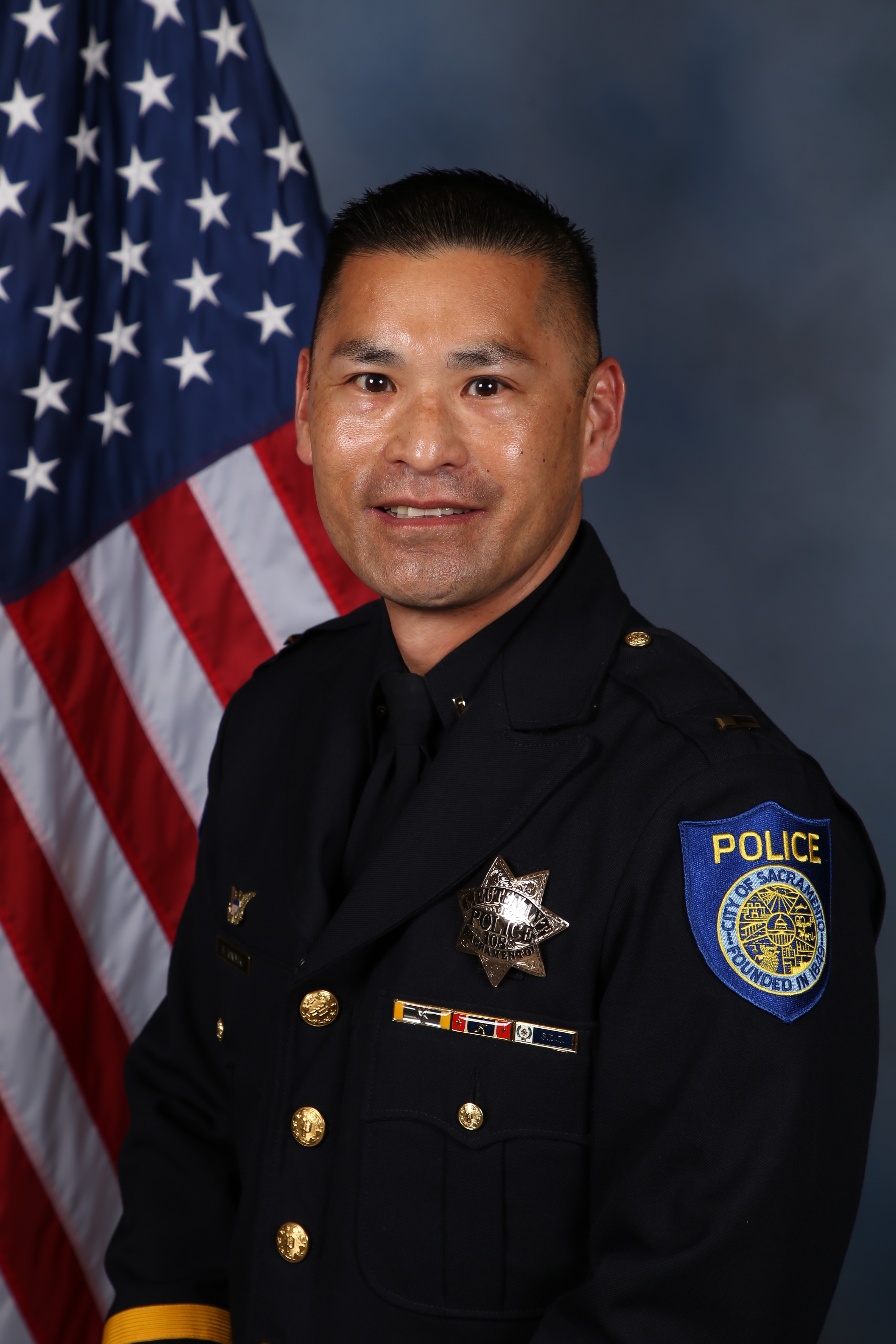Photo of Chief of Brent Kaneyuki in uniform standing in front of the American flag.