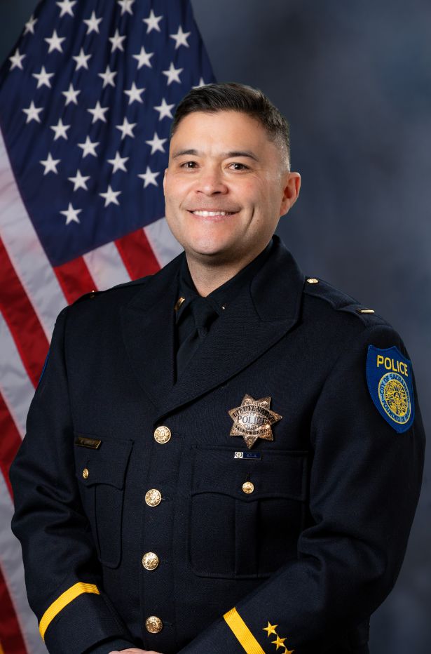 Photo of Ryan Enkoji in uniform standing in front of the American flag.