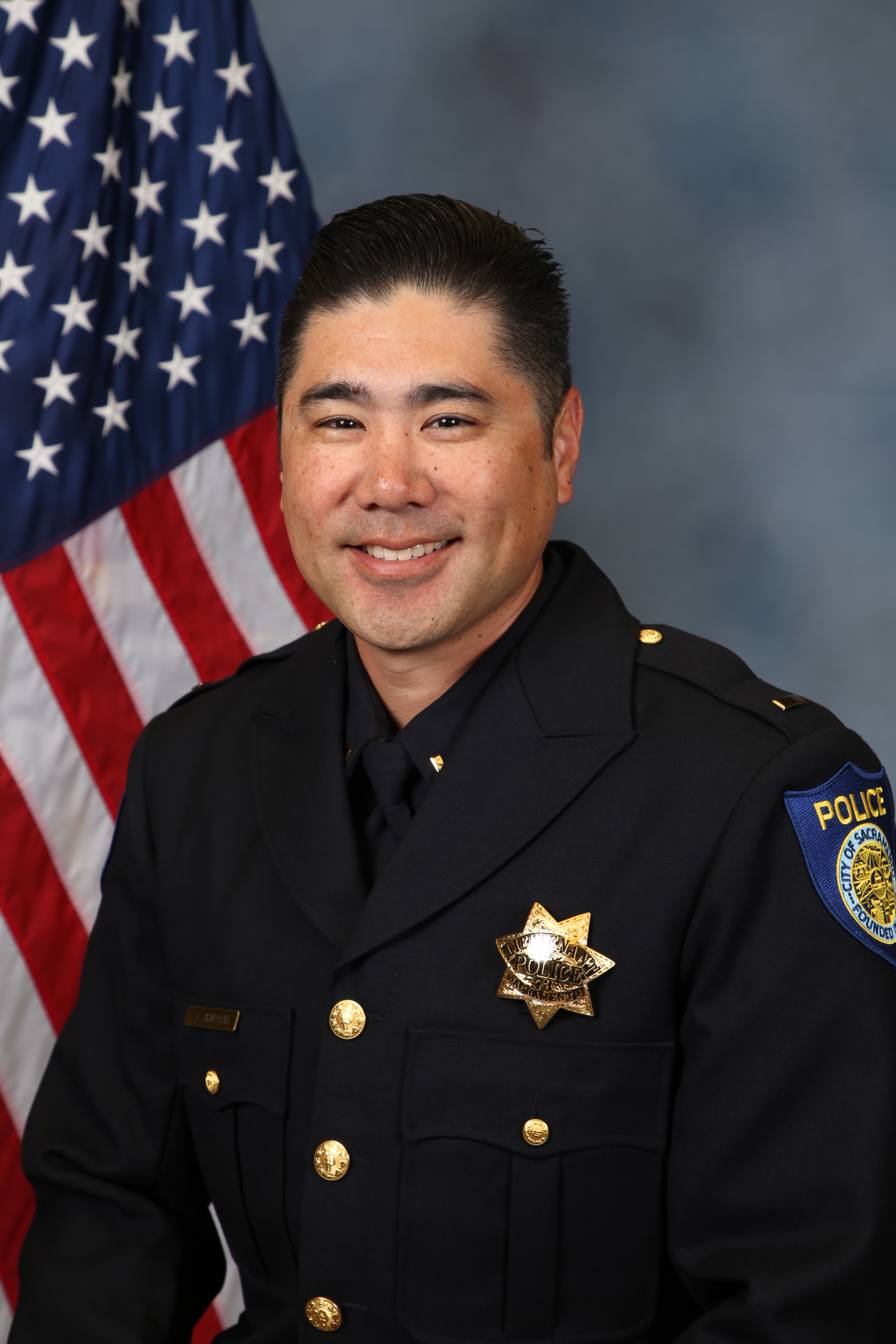 Photo of Jeffrey Shiraishi in uniform standing in front of the American flag.