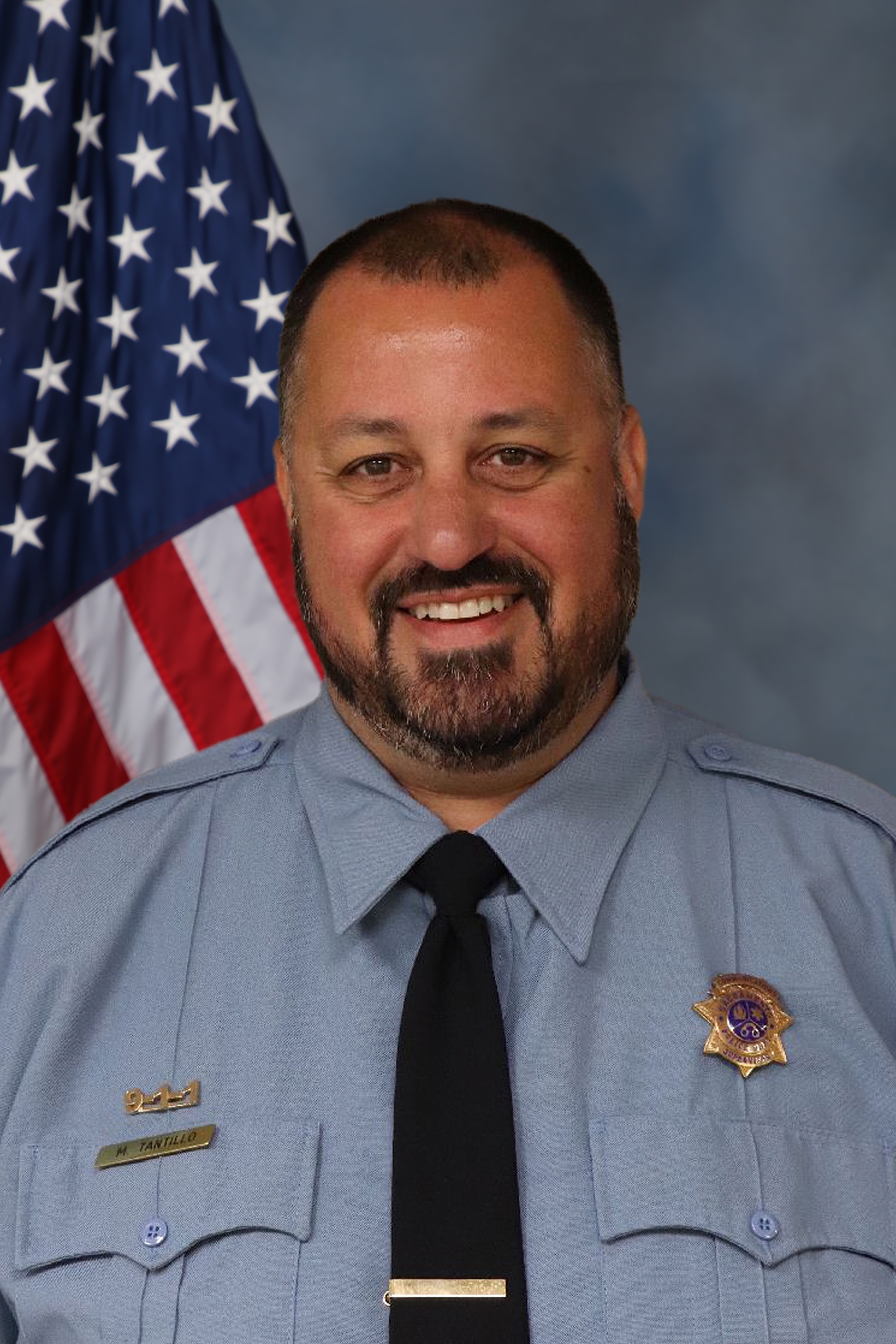 Photo of Marc Tantillo in uniform standing in front of the American flag.