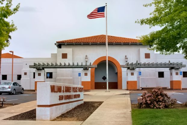 A photo of the Sacramento Police Department's William J. Kinney Police Facility (North Command) . It is a white building with orange trim and roof