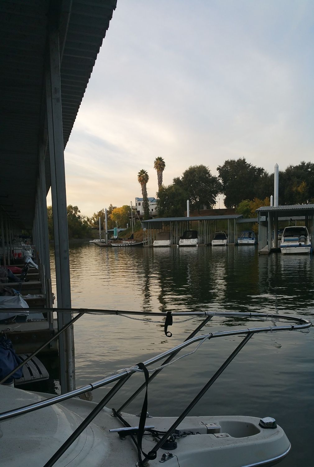 Bow of white boat in a boat slip as image forefront with sun setting in the background