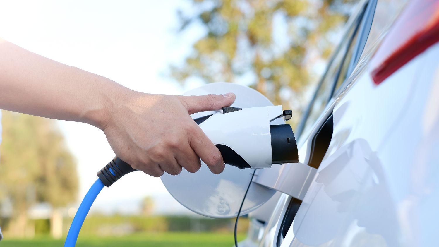 Image of a hand holding an electric vehicle paddle to plug into an electric vehicle