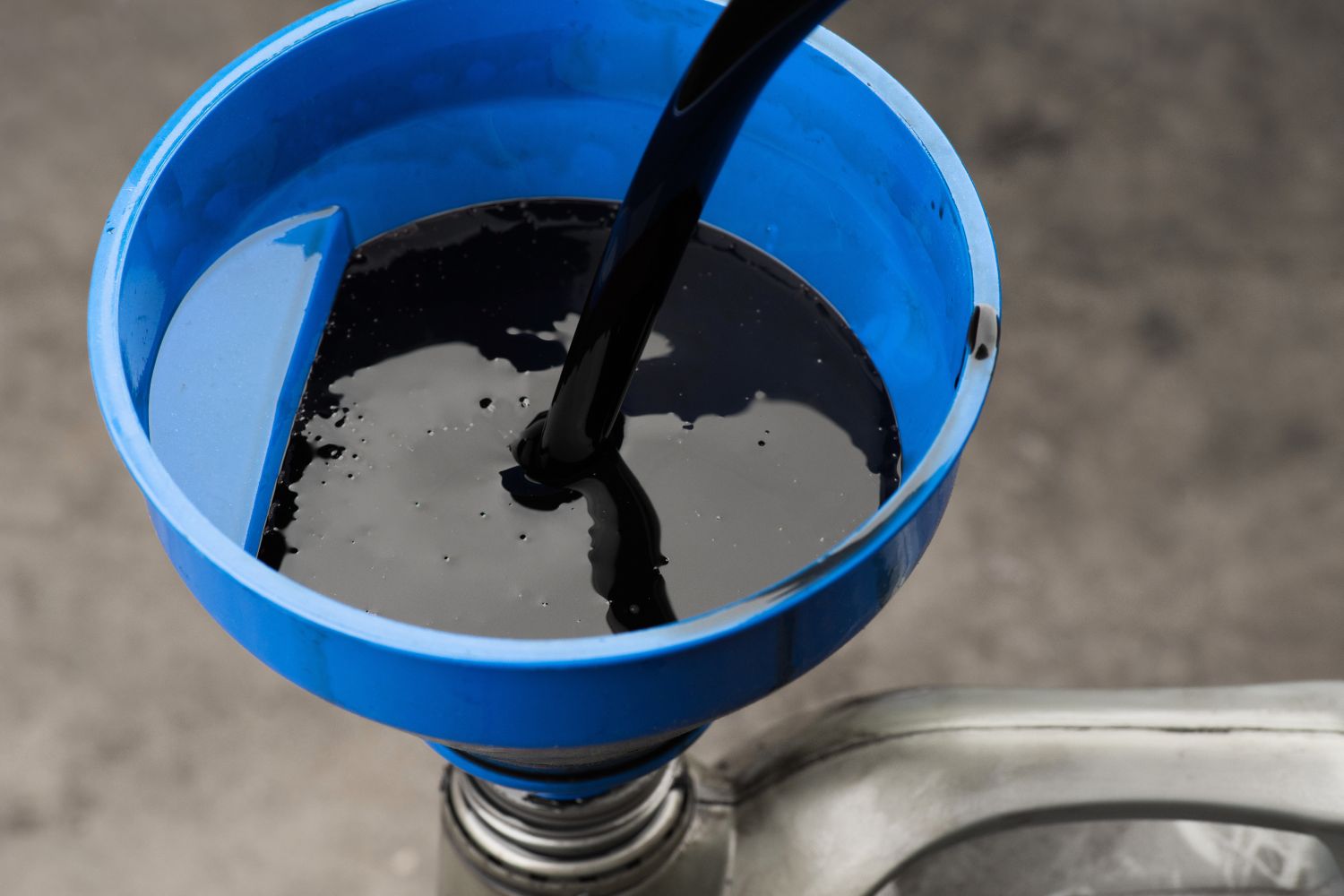 Image of black oil being poured through a blue plastic funnel into a gray plastic container.