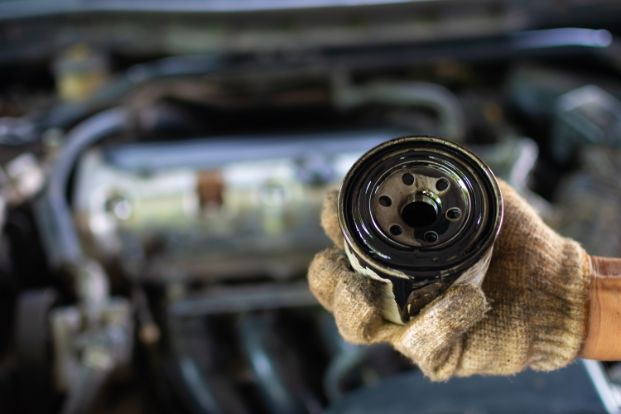 gloved hand holding a used oil filter over an engine