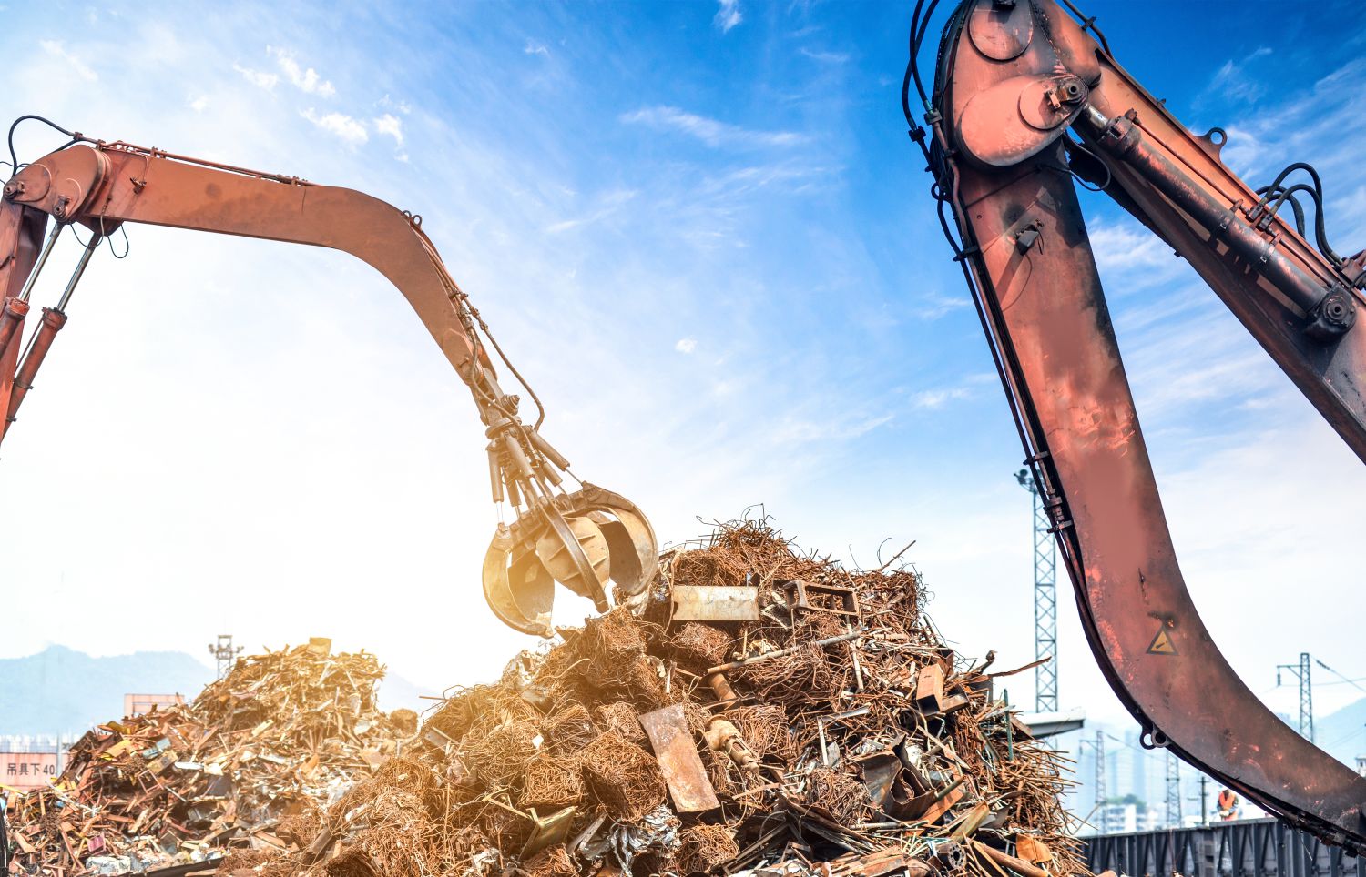 Image of crane with a claw at the end picking up debris from a large junk pile