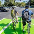 Photo of two people on bicycles waiting in a bicycle left-hand turn pocket at an intersection.