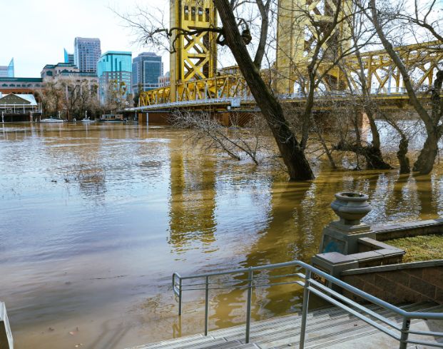 Photo of the Sacramento River flooding a staircase in the West Sacramento River Park Walk, at the Tower Bridge.