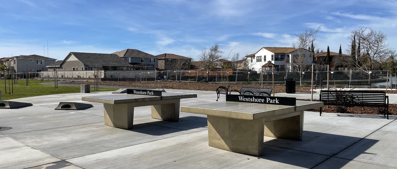 Landscape view of cornhole and ping pong tables at a park.